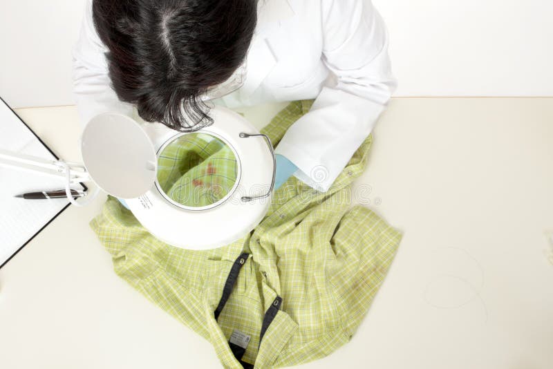 A forensic investigator observes and obtains samples from a shirt for further analysis. A forensic investigator observes and obtains samples from a shirt for further analysis.