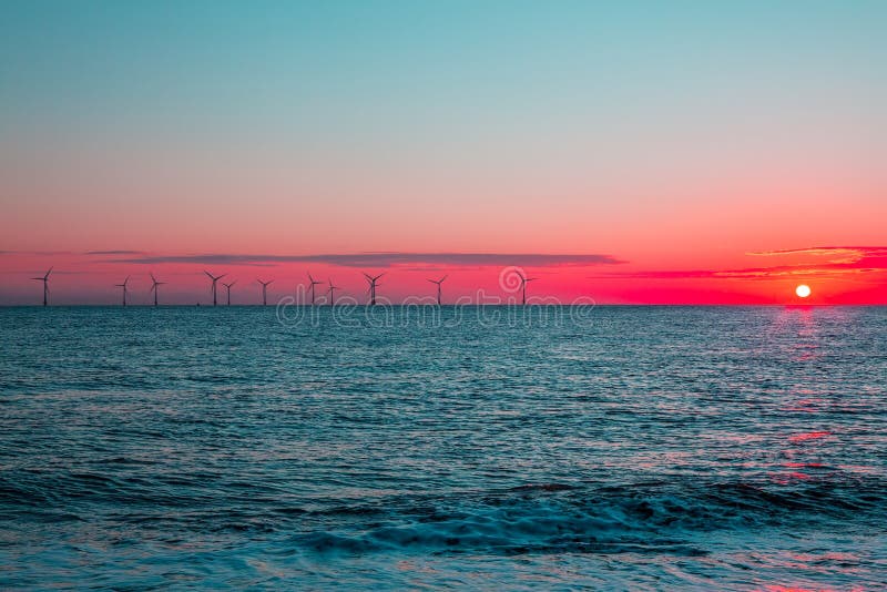 Crimson dawn. Clean energy offshore wind farm turbines at sunrise