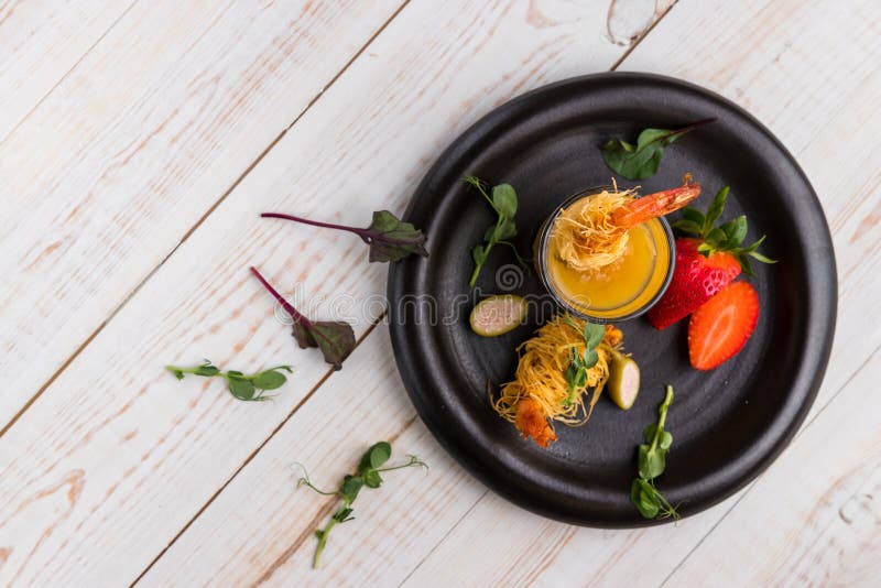 Crispy Shrimp in Kataifi Crust and Thyme with Champagne Sauce in glasses and strawberries lie on a black plate on a white woody stock photo Crispy Shrimp in Kataifi Crust and Thyme with Champagne Sauce in glasses and strawberries lie on a black plate on a white woody stock photo