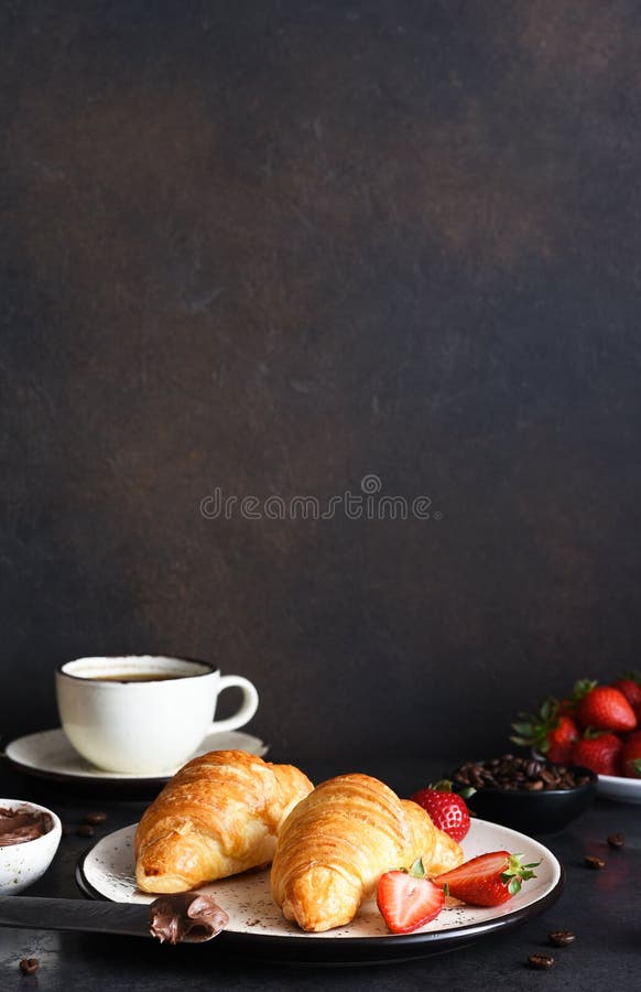 Croissant with chocolate paste and a cup of coffee, strawberries on the kitchen table. â€‹Traditional snack or breakfast