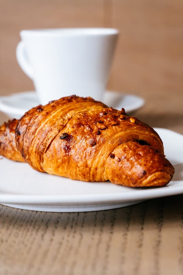 Croissant Filled with Chocolate and Decorated with Hazelnuts, at the Bottom Cup of Hot Coffee