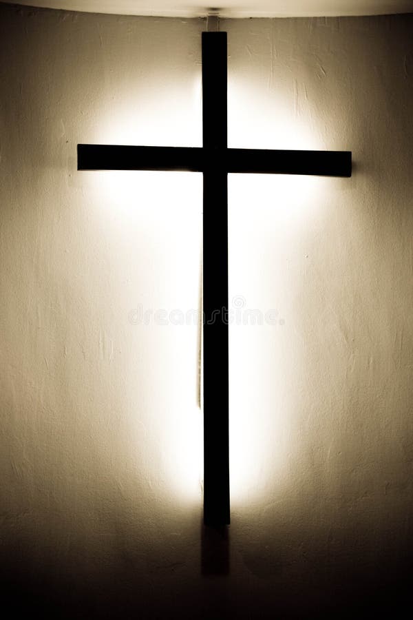 A wooden black cross mouted on a wall with bright light behind the cross. A wooden black cross mouted on a wall with bright light behind the cross