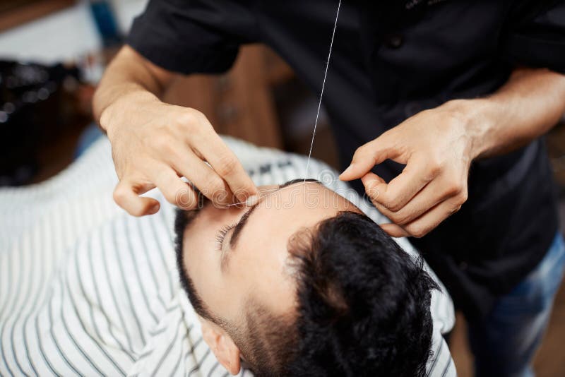 Crop barber threading eyebrows of client stock photo