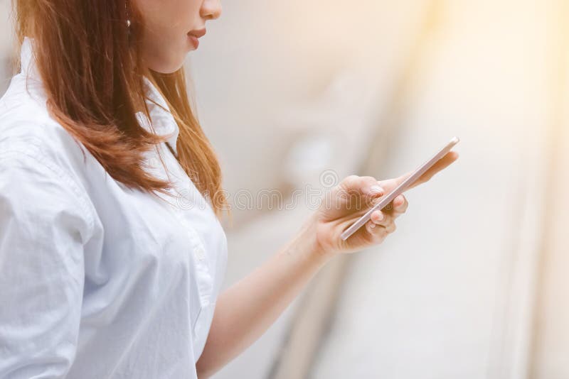 Cropped image of attractive young Asian woman holding mobile smart phone on the street of city with sunshine effect. Social stock photography Cropped image of attractive young Asian woman holding mobile smart phone on the street of city with sunshine effect. Social stock photography