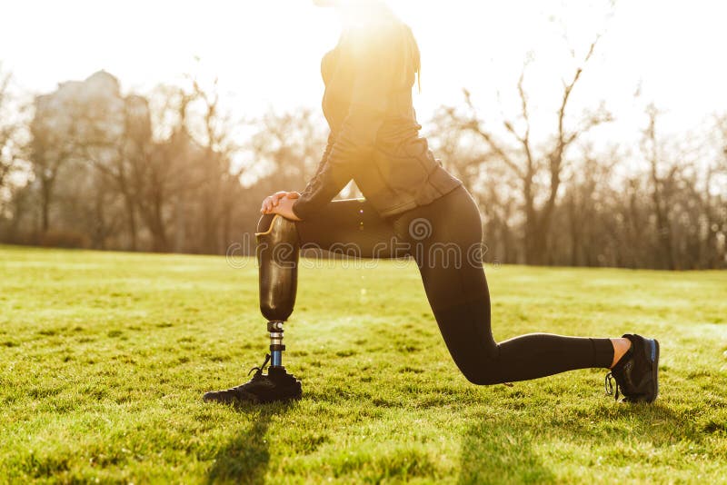 Cropped image of disabled athletic girl in black sportswear, doing lunges and stretching prosthetic leg on grass royalty free stock images Cropped image of disabled athletic girl in black sportswear, doing lunges and stretching prosthetic leg on grass royalty free stock images