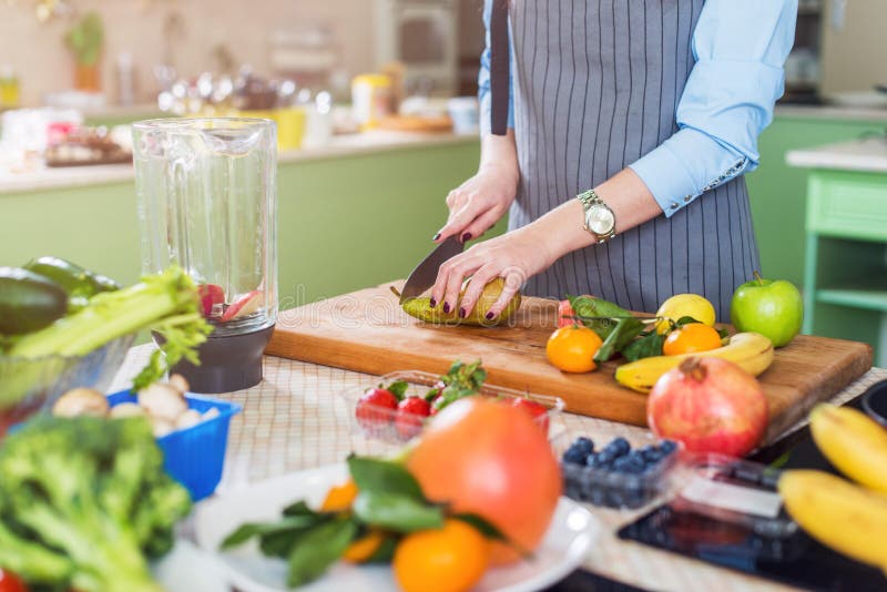 Cropped image of female cook cutting fruit on board preparing smoothie in kitchen royalty free stock photography Cropped image of female cook cutting fruit on board preparing smoothie in kitchen royalty free stock photography