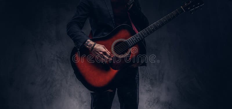 Cropped image of a musician in elegant clothes with a guitar in his hands playing and posing.