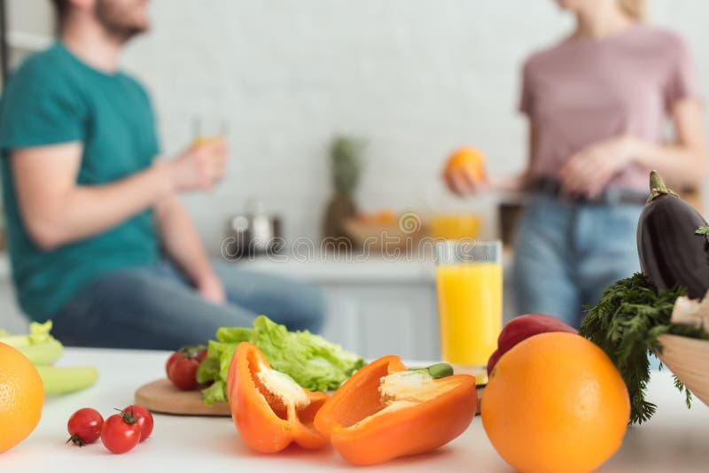 cropped image of vegan couple talking in kitchen with fruits and vegetables