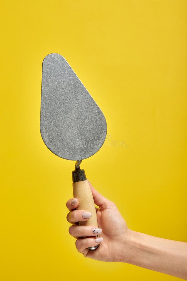 cropped male holding spatula in hands, for cleaning a concrete wall from defects, repair and construction, surface preparation, on yellow background, copy space