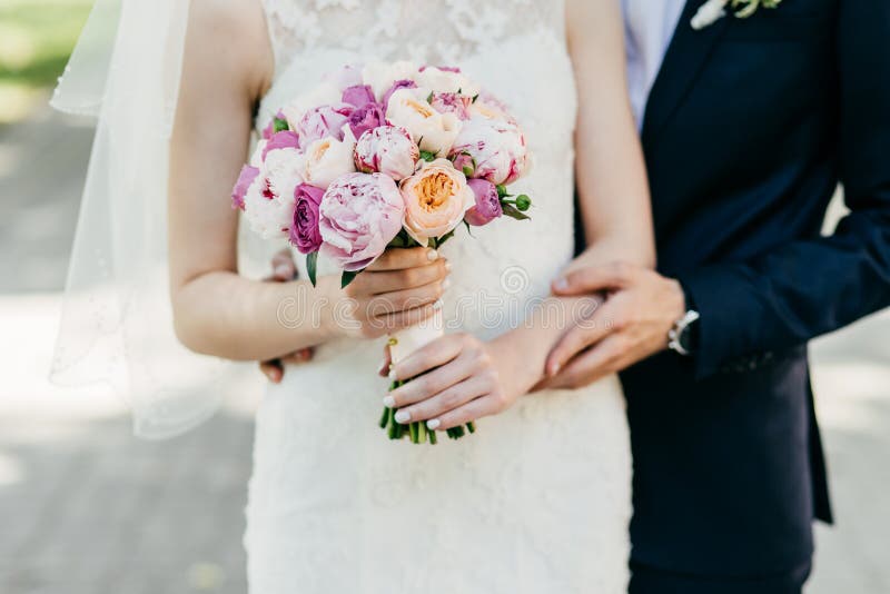 Cropped shot of beautiful bride in white wedding dress holding bouquet standing near groom who is hugging her from behind. Happy n royalty free stock photography Cropped shot of beautiful bride in white wedding dress holding bouquet standing near groom who is hugging her from behind. Happy n royalty free stock photography