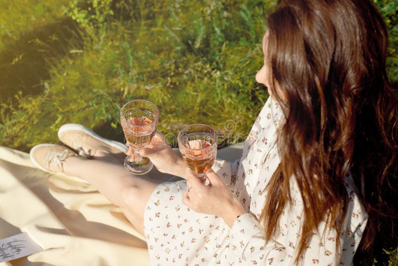 Cropped shot of a girl, in a summer dress, sitting with a glass of wine at a picnic while enjoying a picnic outdoors