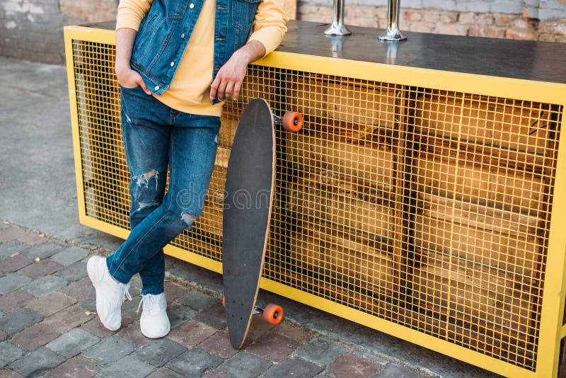 cropped shot of man with longboard standing. Clothing, daytime.