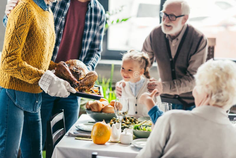 cropped shot of man and woman carrying turkey for thanksgiving dinner while excited family looking