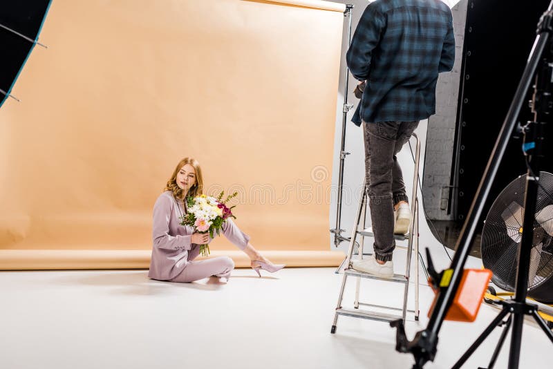 Cropped shot of photographer standing on step ladder while beautiful girl posing with bouquet of flowers