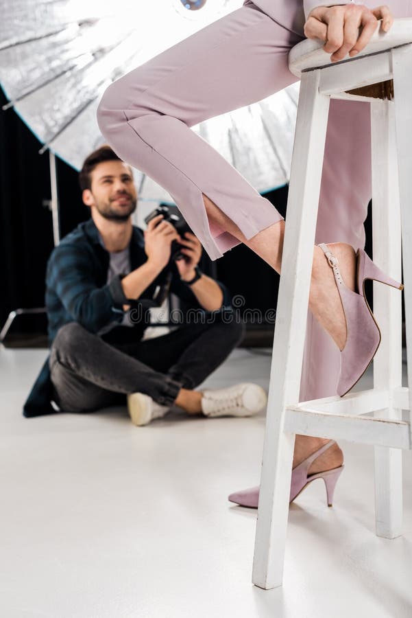 cropped shot of smiling photographer sitting and photographing stylish female model