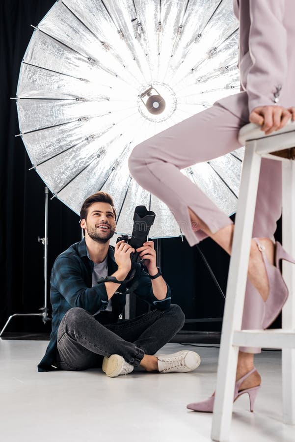 cropped shot of smiling photographer sitting and photographing stylish model