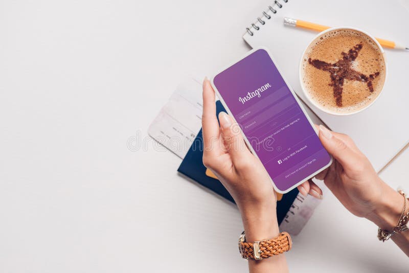 cropped shot of woman with smartphone with instagram logo on screen at tabletop with cup of coffee ticket and passport