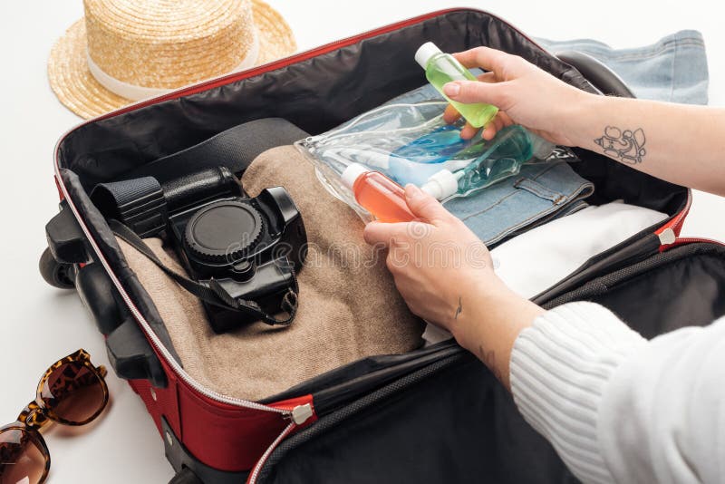 Cropped view of woman packing travel bag with cosmetic bag with colorful bottles.