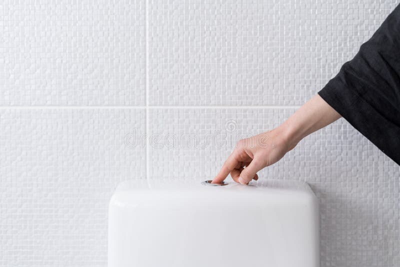 Woman`s hand pushing button and flushing toilet