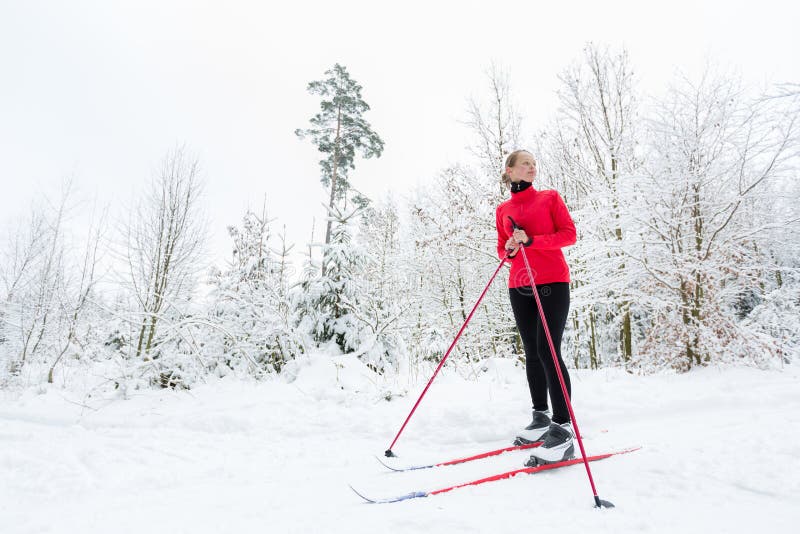 Cross-country skiing: young woman cross-country skiing on a winter day, taking a break to apreciate the snowy forest environment (color toned image)