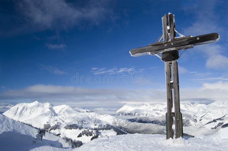 Cross on a snow covered mountain summit in winter with blue sky and copy space. Cross on a snow covered mountain summit in winter with blue sky and copy space