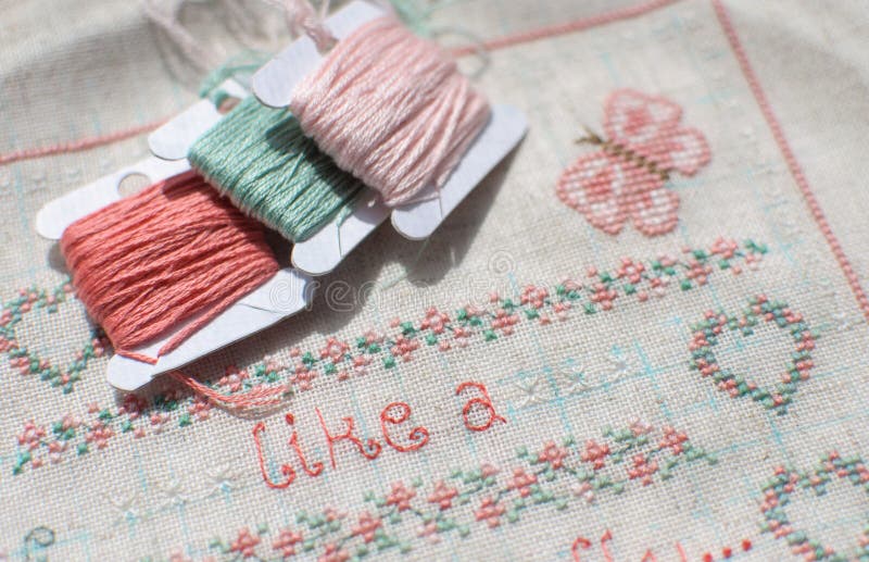 Crossstitch Embroidery on Linen and Three Bobbins of Thread. Stock