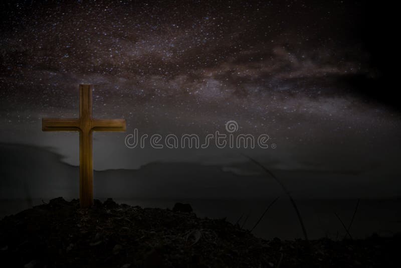 Cross wooden raised to the glory of God, Jesus Christ. Night light lighting a fire on a background of stones under the stars of th