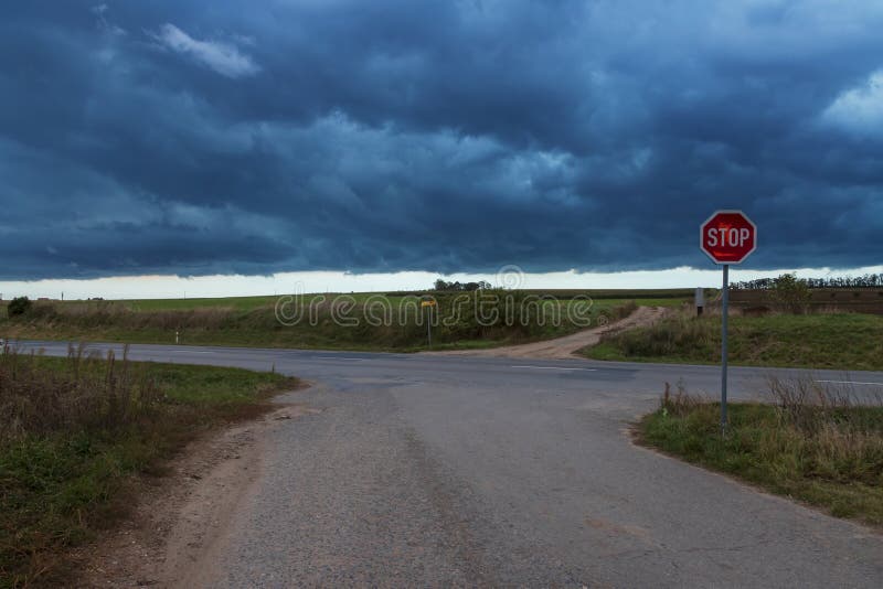 Crossroads on the road. The STOP road sign is visible. In the background is a dramatic sky with clouds