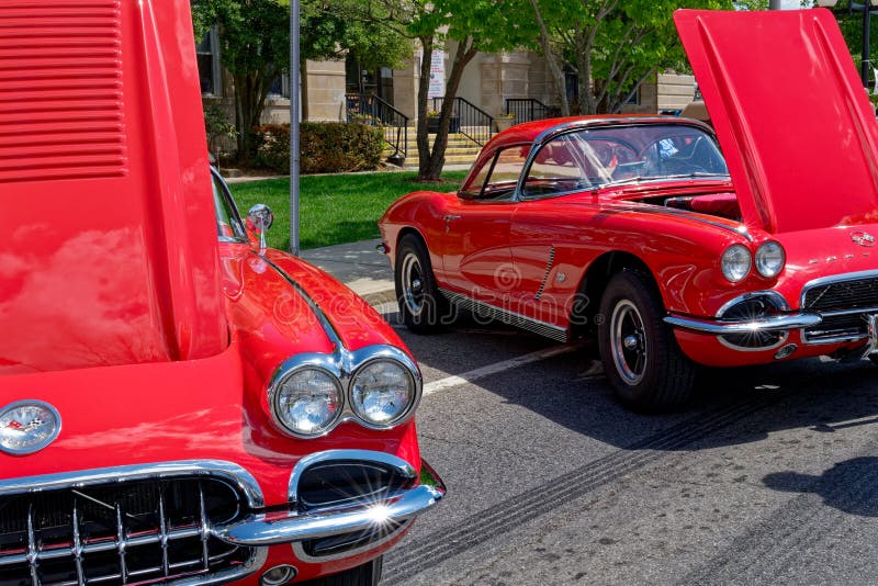 Partial view of two 1960's red Chevrolet Corvettes with the hoods up alongside on main street at a vintage car show on a sunny day in springtime. Partial view of two 1960's red Chevrolet Corvettes with the hoods up alongside on main street at a vintage car show on a sunny day in springtime