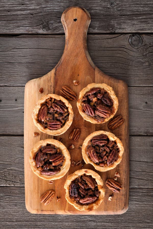 Crostate della crostata di noci di pecan su un bordo di pagaia di legno fotografia stock Crostate della crostata di noci di pecan su un bordo di pagaia di legno fotografia stock