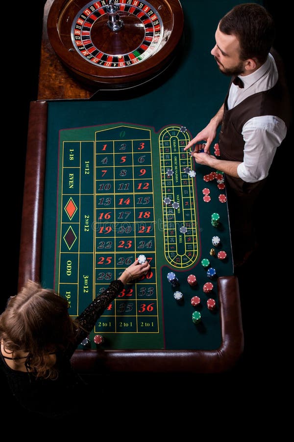 Croupier- och kvinnaspelare på en tabell i en kasino Bild av A.C. royaltyfri foto Croupier- och kvinnaspelare på en tabell i en kasino Bild av A.C. royaltyfri foto