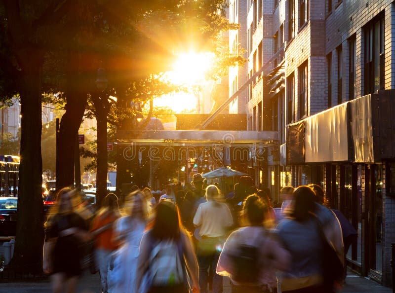 Crowds of diverse people walking down the sidewalks of 14th Street with the bright light of summer sunset shining above in New