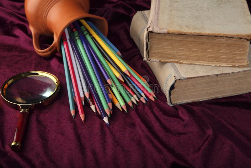 Cruche retournée avec les crayons colorés, la loupe et les vieux livres sur le bureau Vue stylisée de rétros objets photo stock Cruche retournée avec les crayons colorés, la loupe et les vieux livres sur le bureau Vue stylisée de rétros objets photo stock