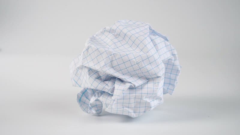 A crumpled ball of empty squared paper sheet falls on the white surface of the table