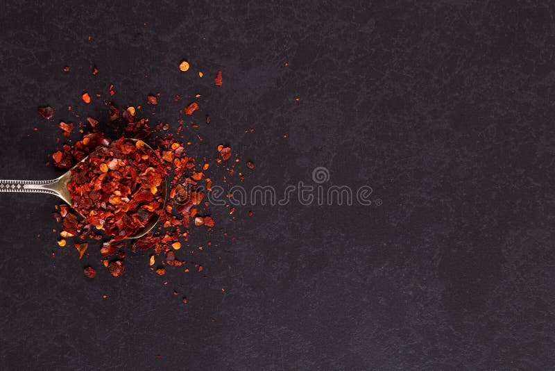Crushed dried chili peppers in an iron spoon scattered on a black background. Concept, copy space stock photos