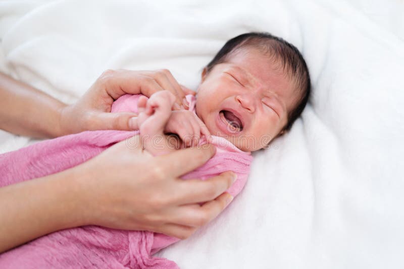 Crying Newborn Baby Wrap in Blanket and Parent Hands on Bed Stock Photo