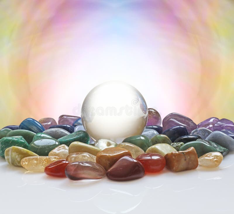 Large clear crystal ball with a selection of chakra colored healing crystals and a pastel colored background plus plenty of copy space. Large clear crystal ball with a selection of chakra colored healing crystals and a pastel colored background plus plenty of copy space