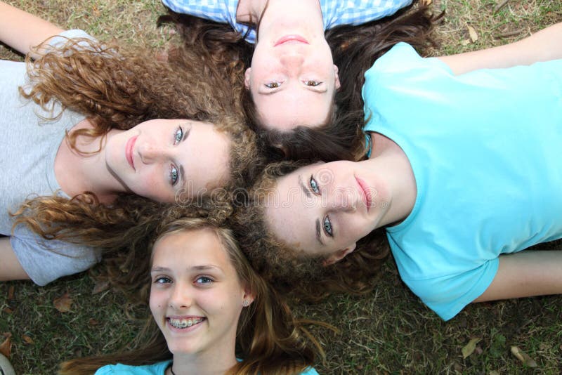 Four beautiful teenage female friends lying on their backs with their heads close together smiling up as they enjoy their summer vacation together. Four beautiful teenage female friends lying on their backs with their heads close together smiling up as they enjoy their summer vacation together