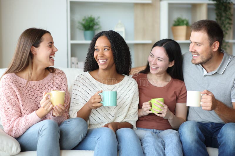 Cuatro amigos interraciales hablando en casa y bebiendo imágenes de archivo libres de regalías