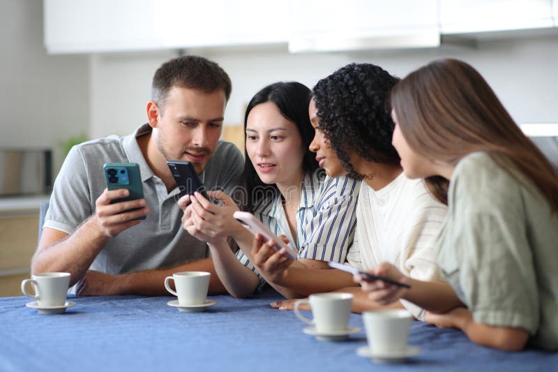 Cuatro amigos interraciales revisando sus teléfonos móviles foto de archivo libre de regalías