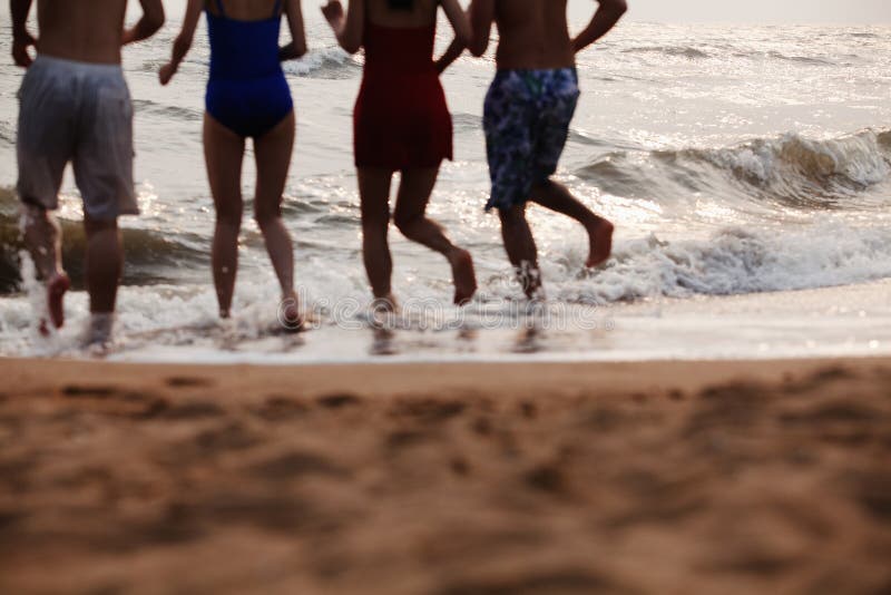 Cuatro amigos que corren en el agua en una playa arenosa, silueta fotografía de archivo Cuatro amigos que corren en el agua en una playa arenosa, silueta fotografía de archivo