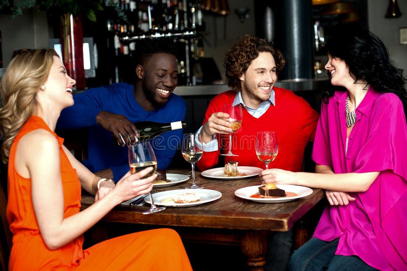 Cuatro amigos que disfrutan de la cena en un restaurante imagenes de archivo Cuatro amigos que disfrutan de la cena en un restaurante imagenes de archivo