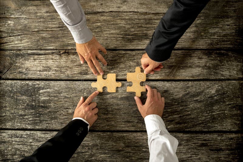 Four successful business men joining two puzzle pieces each being held by two partners, rustic wooden background. Conceptual of merger or creative cooperation of two business companies. Four successful business men joining two puzzle pieces each being held by two partners, rustic wooden background. Conceptual of merger or creative cooperation of two business companies.