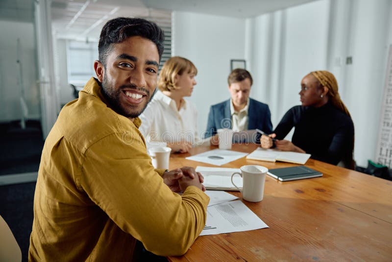 Four happy young multiracial adults wearing businesswear talking in meeting room at office. Four happy young multiracial adults wearing businesswear talking in meeting room at office