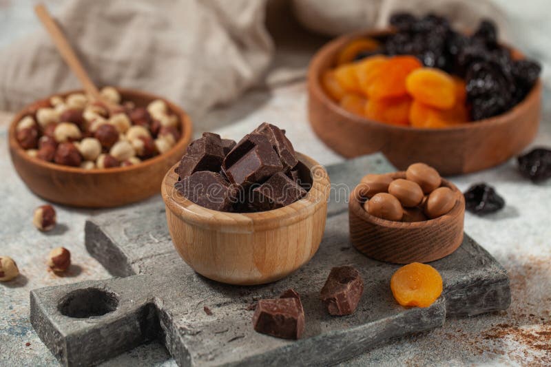 Cubes of dark artisan chocolate. Assorted nuts, dark chocolate, and dried fruits on stone, an artisanal feast for the senses.