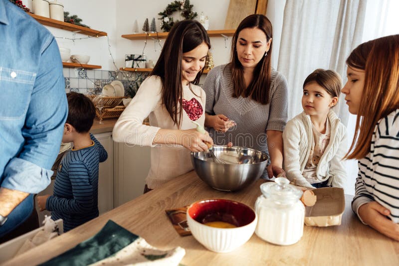 Cucinare una cena festiva con tutta la famiglia in cucina. una ragazza batte uova in una ciotola di metallo. la mamma la aiuta immagini stock libere da diritti
