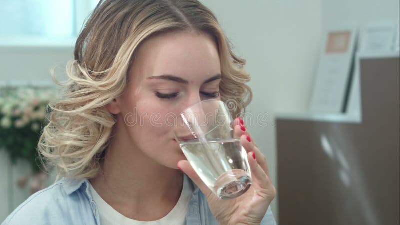 Cudowna młoda kobieta zdrowieje pijąc szklankę wody w pomieszczeniach i uśmiechając się zbiory