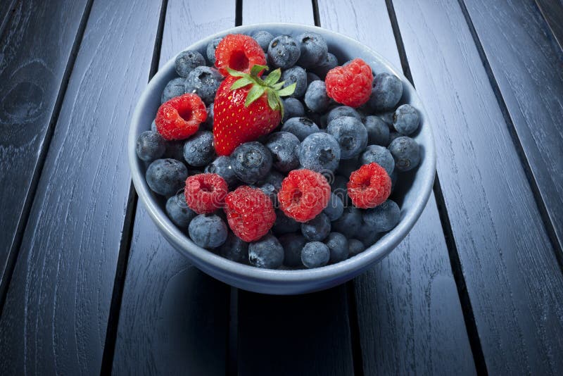 A bowl of fresh summer berries on a black wood background. A bowl of fresh summer berries on a black wood background