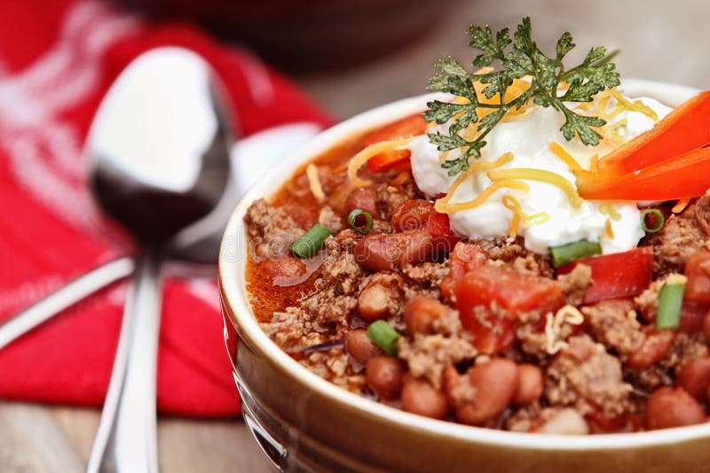 Bowl of Chili Con Carne garnished with sour cream, chives and cheddar cheese. Extreme shallow depth of field with selective focus on center of bowl. Bowl of Chili Con Carne garnished with sour cream, chives and cheddar cheese. Extreme shallow depth of field with selective focus on center of bowl.