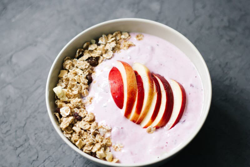 Cuenco de gachas de avena de la harina de avena con el yogur de arándano, la leche y el muesli con una manzana en fondo concreto foto de archivo libre de regalías Cuenco de gachas de avena de la harina de avena con el yogur de arándano, la leche y el muesli con una manzana en fondo concreto foto de archivo libre de regalías